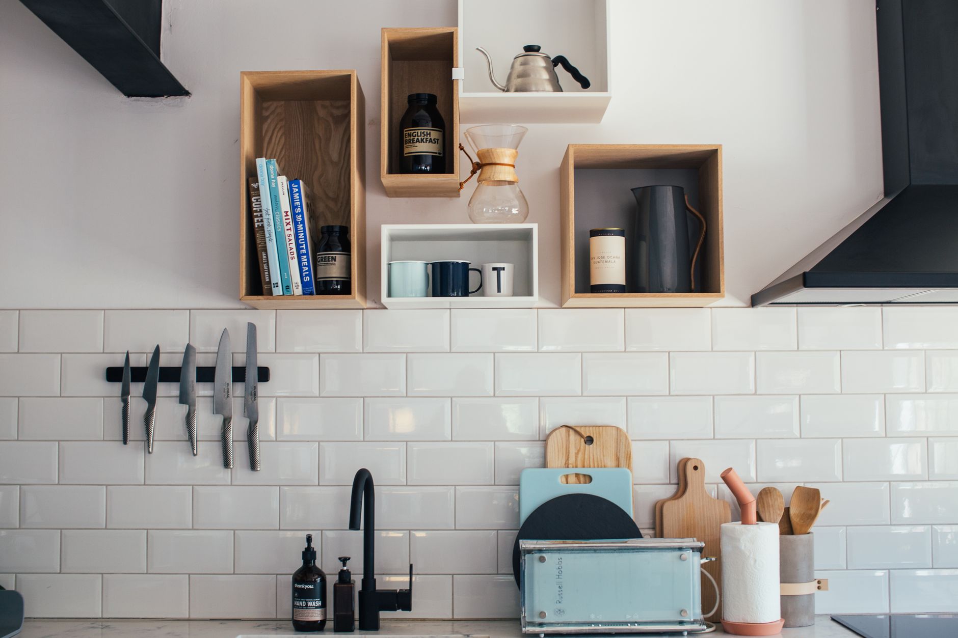 Chemex and coffee kettle with books and cups placed on wooden shelves hanging on wall over sink in kitchen