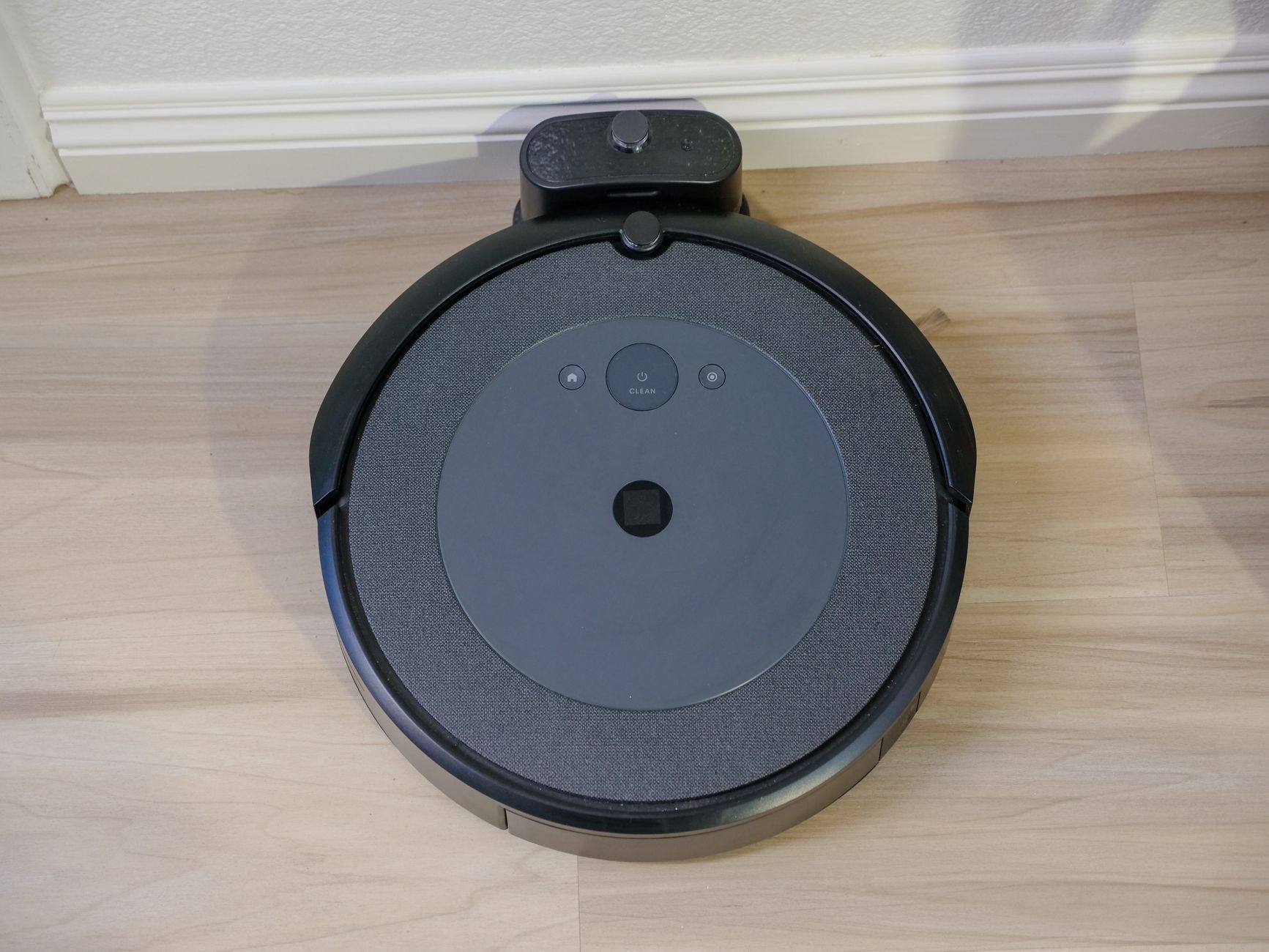 Compact automatic robovac on a wooden floor from above view.