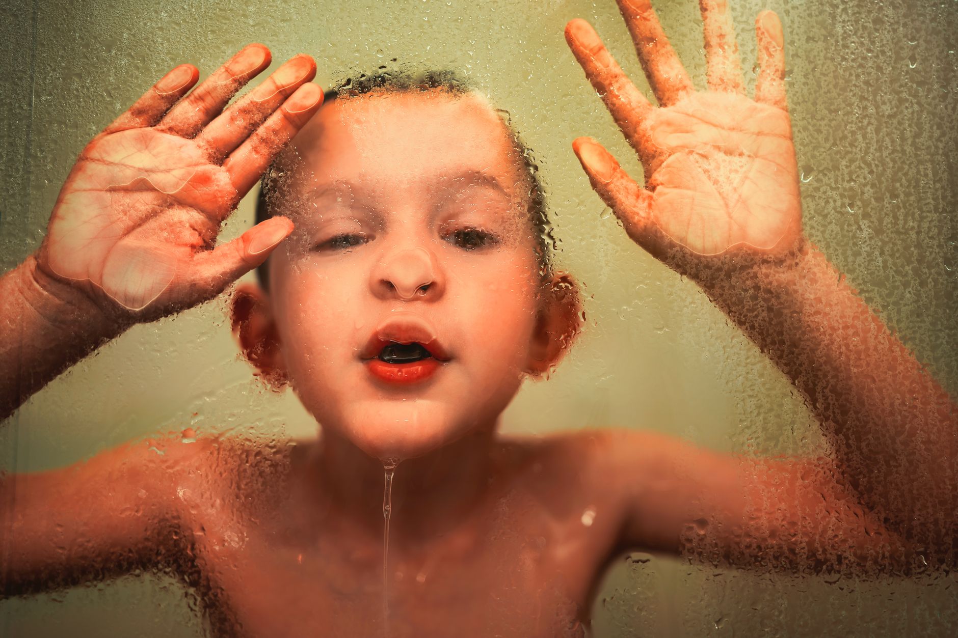 A young child playfully presses their face against a shower door, showcasing joy and innocence.