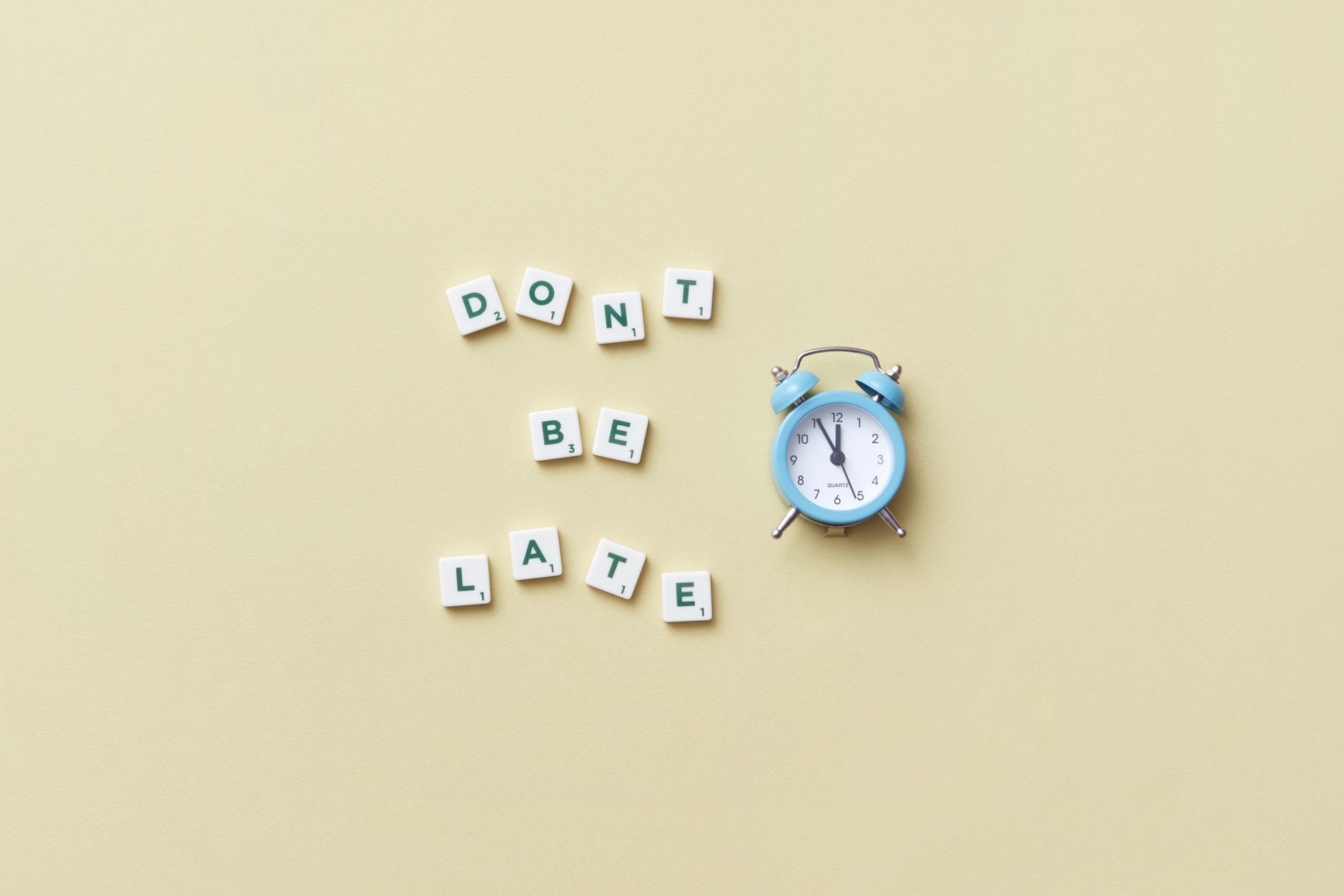 Flat lay of a blue alarm clock and letter tiles spelling 'Don't Be Late'.