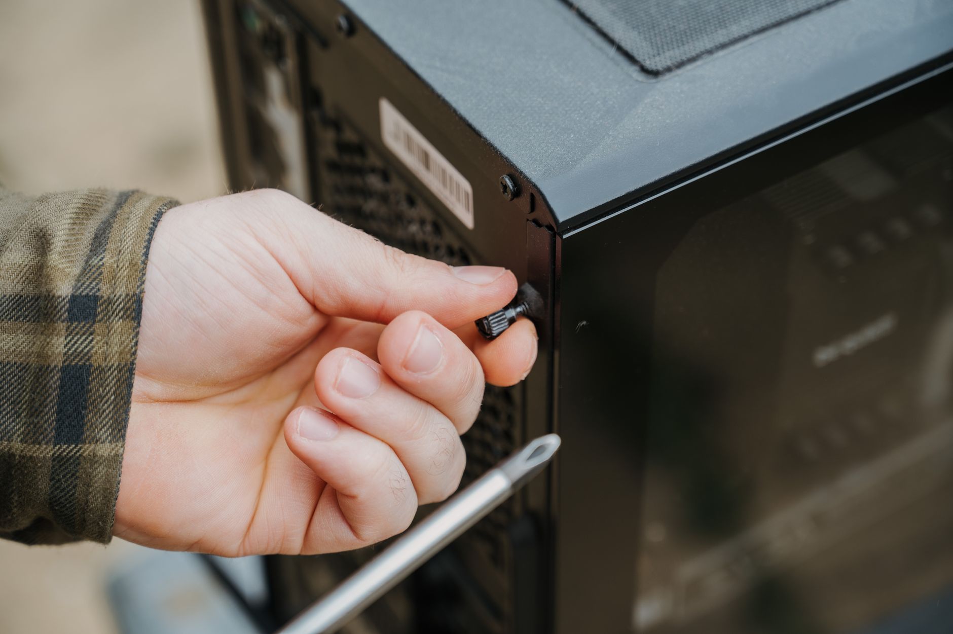 Close-up of a hand unscrewing a desktop computer case, emphasizing technology maintenance.