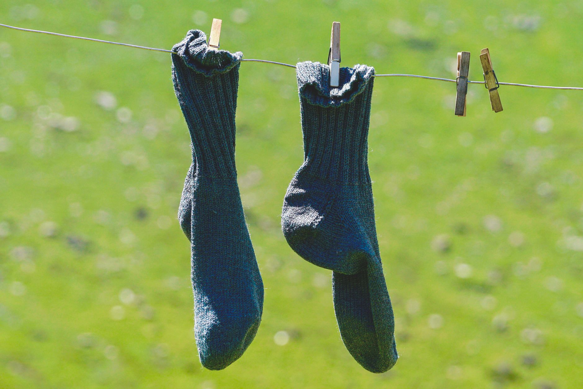 Woolen socks hung on a clothesline, drying in the sun with a natural green backdrop.