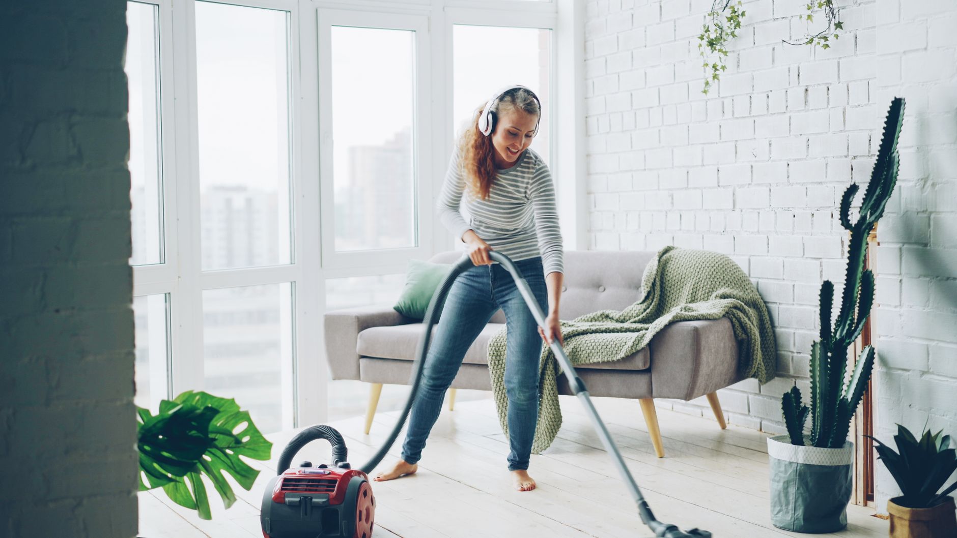 Woman vacuuming a stylish living room while listening to music on headphones, enjoying the chore.