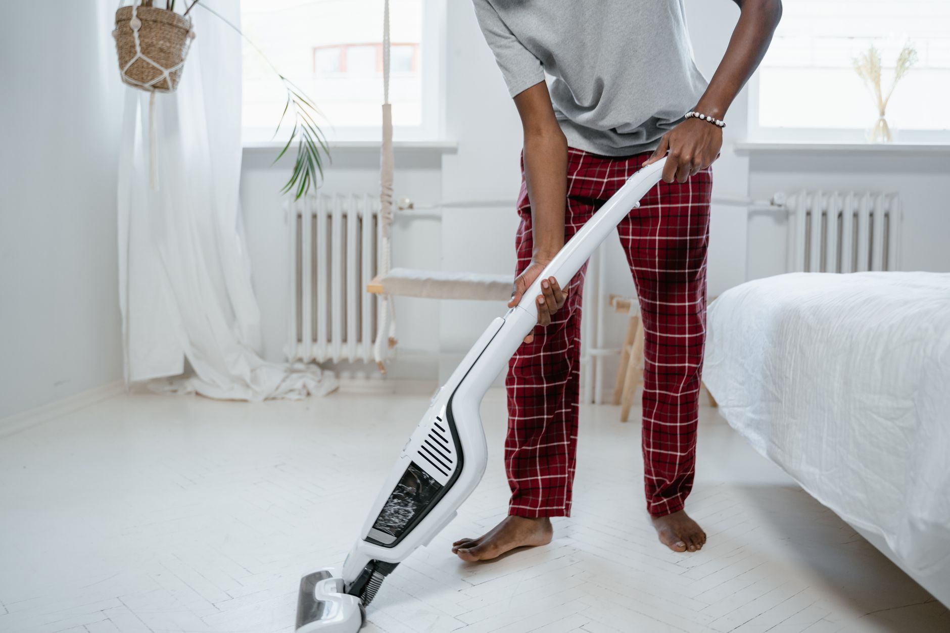 A person cleaning a bedroom with a modern vacuum cleaner, showcasing casual home lifestyle.