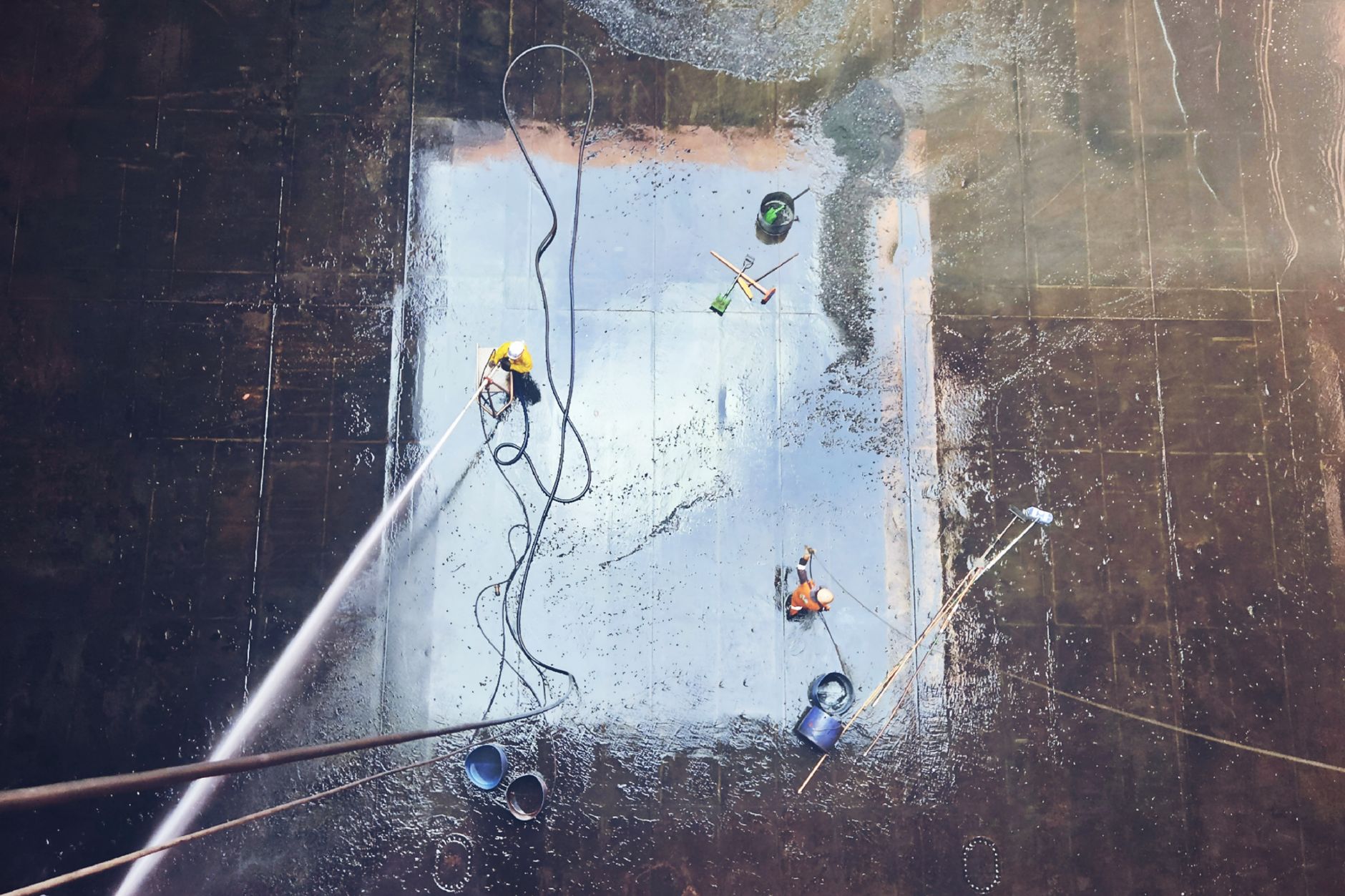 Top view of workers cleaning a large surface with equipment and water hoses.