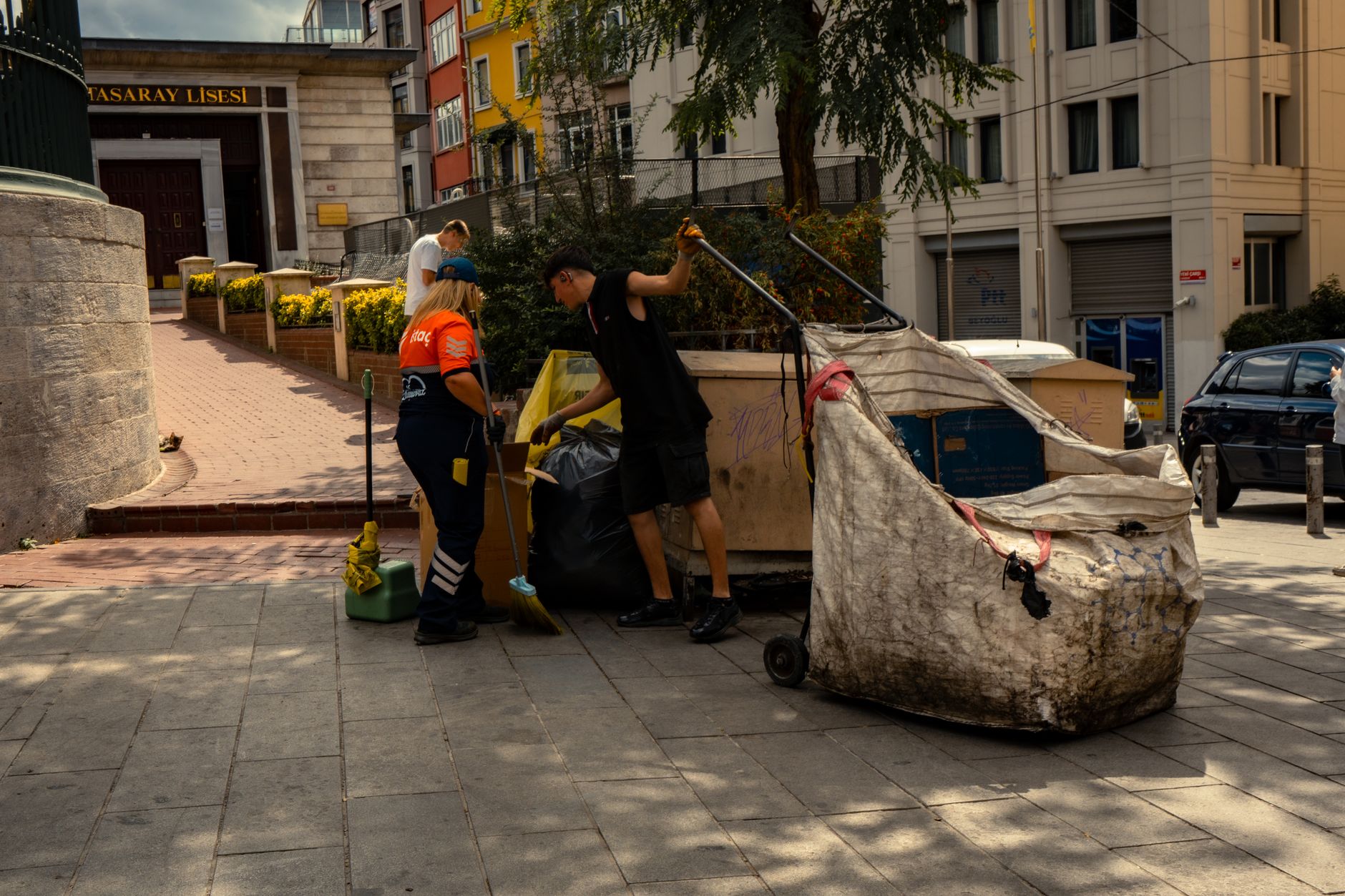 Two sanitation workers collecting waste on a sunny day in the city.