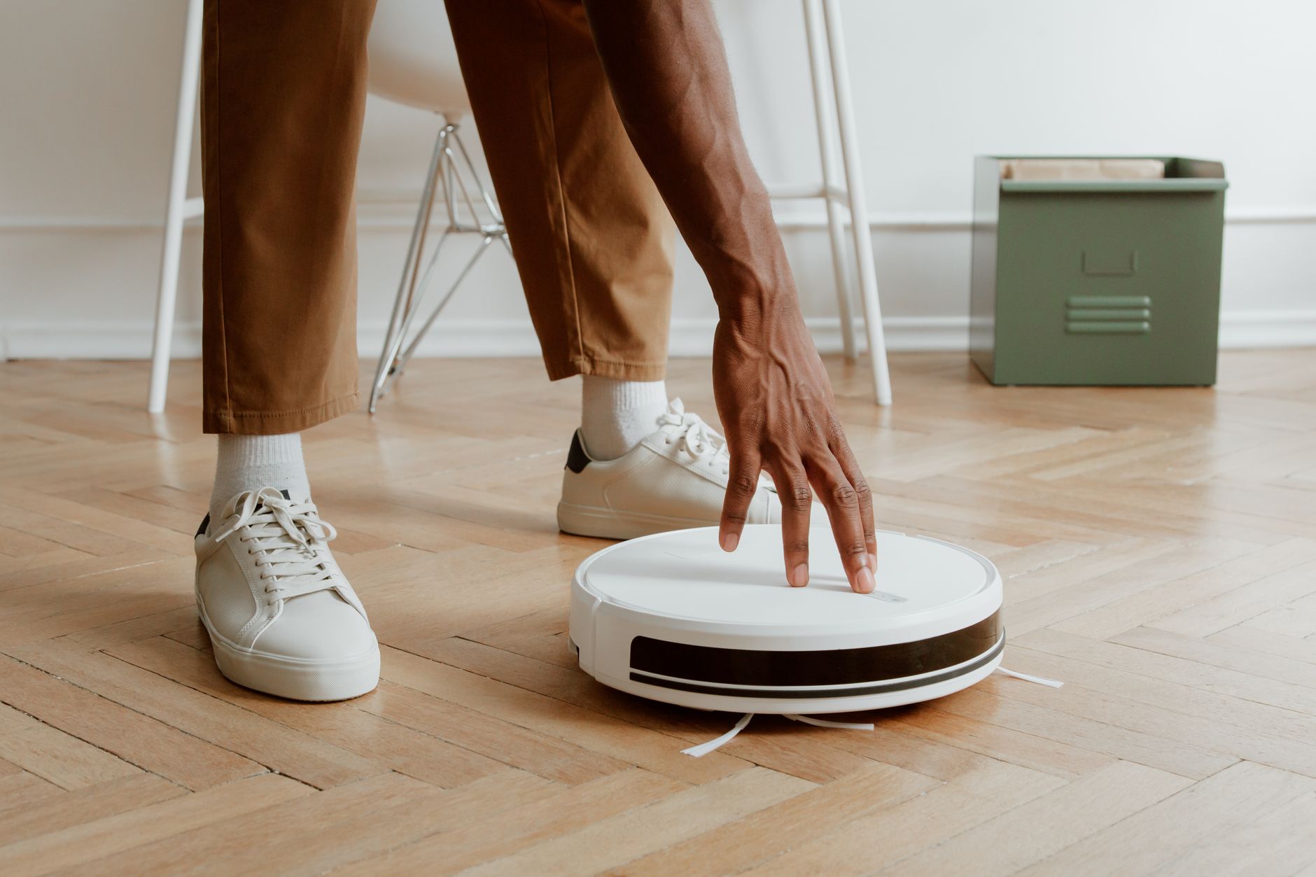 A man's hand adjusting a robot vacuum on a wooden floor in a modern home interior.