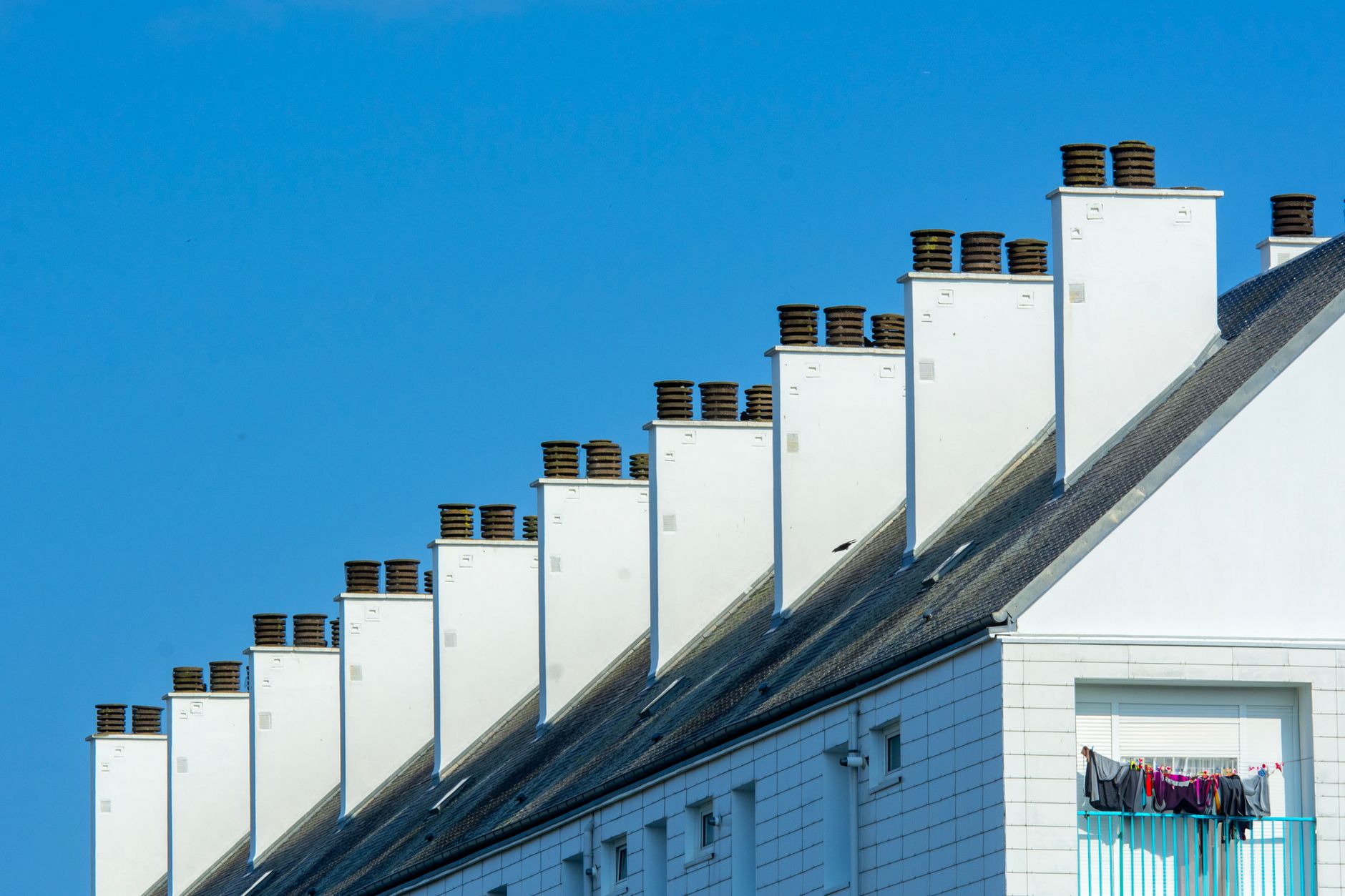 Row of chimneys on modern residential buildings under a clear blue sky. Urban architecture with rooftops.