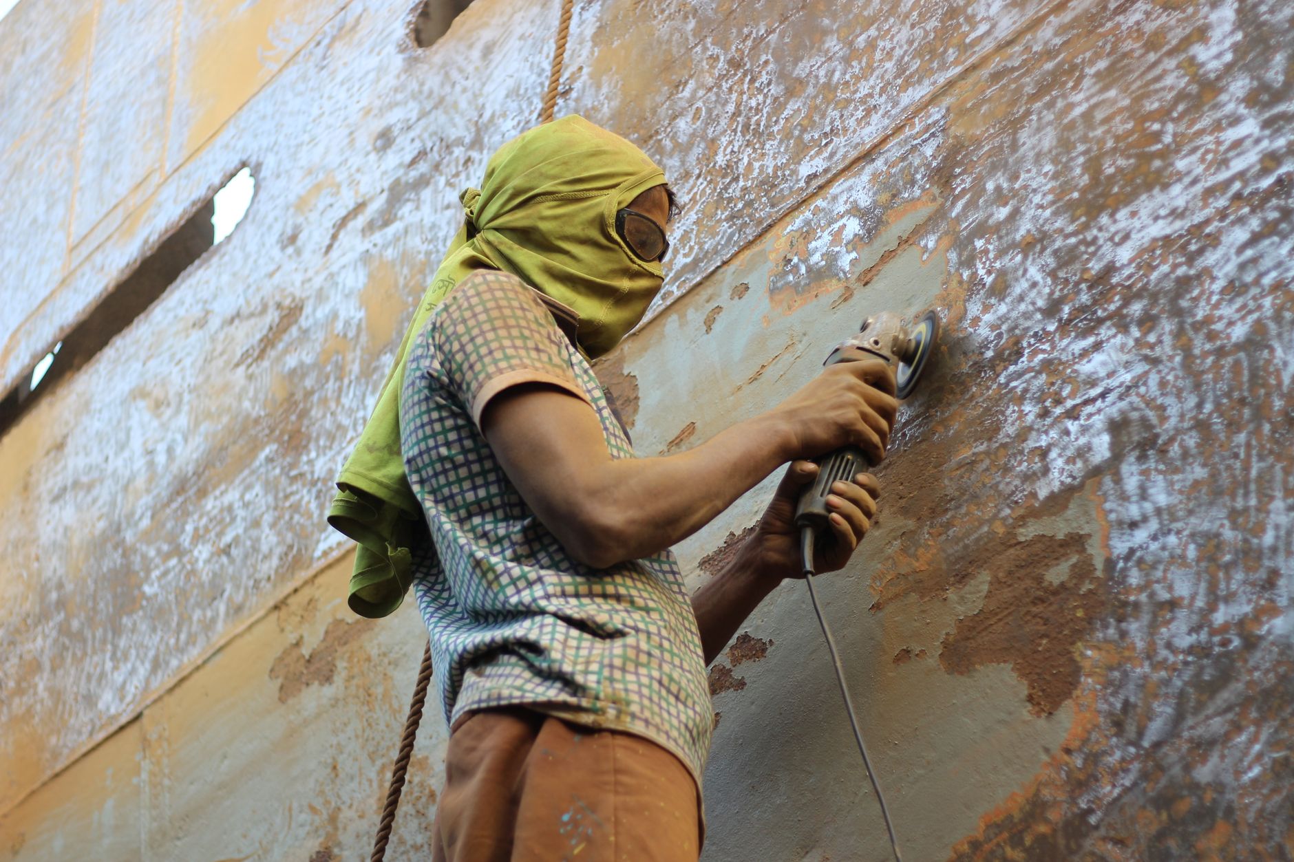 A worker using a grinder to polish rusted metal, wearing protective clothing outdoors.
