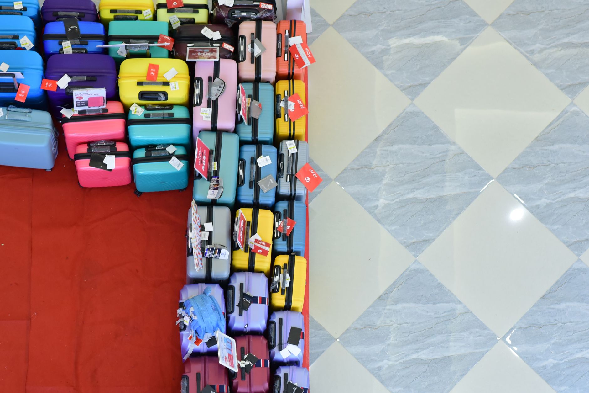 Top view of vibrant suitcases arranged on a checkered floor for sale.