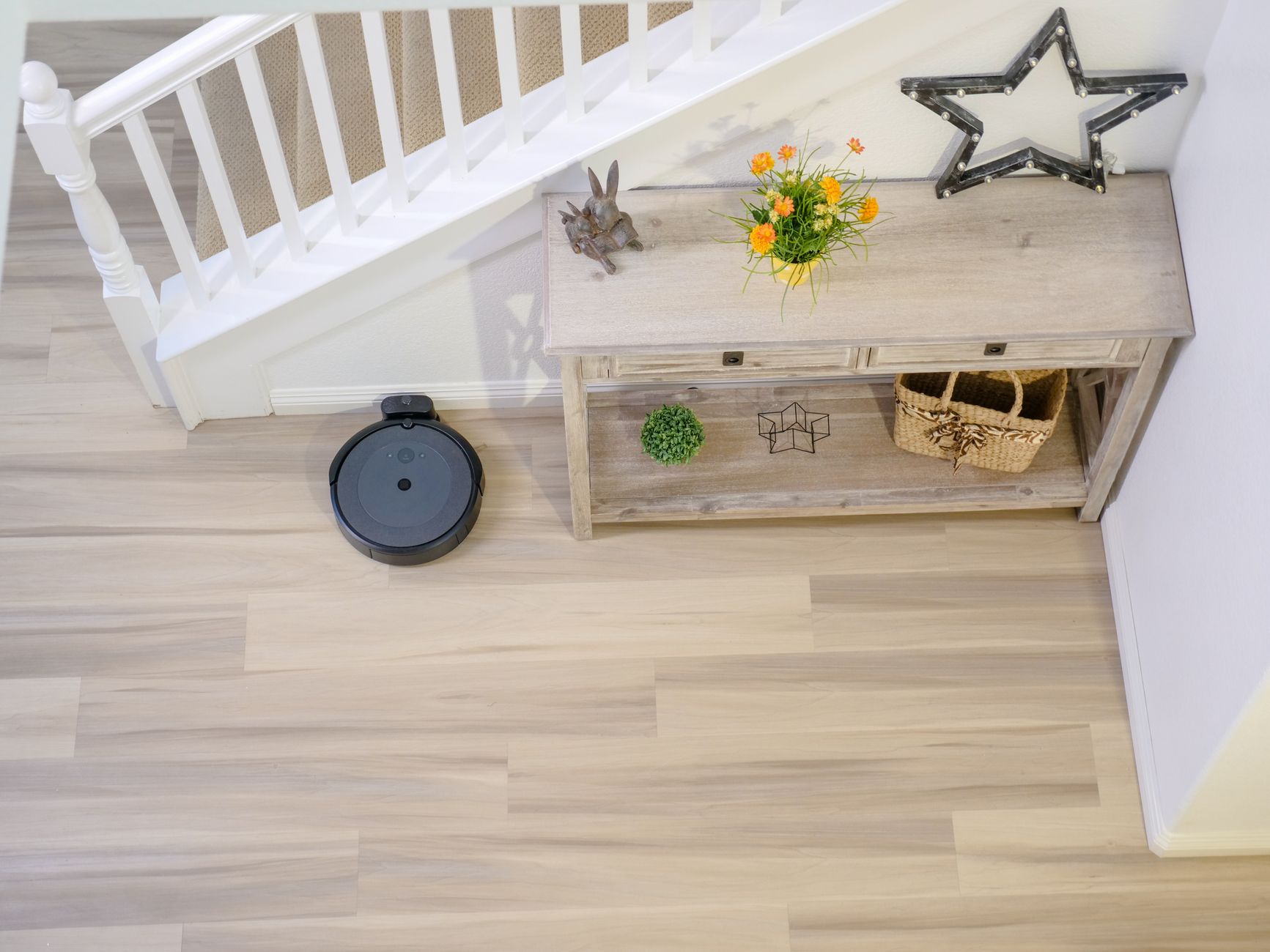 An autonomous robovac cleaning a wooden floor next to a decorative console table.