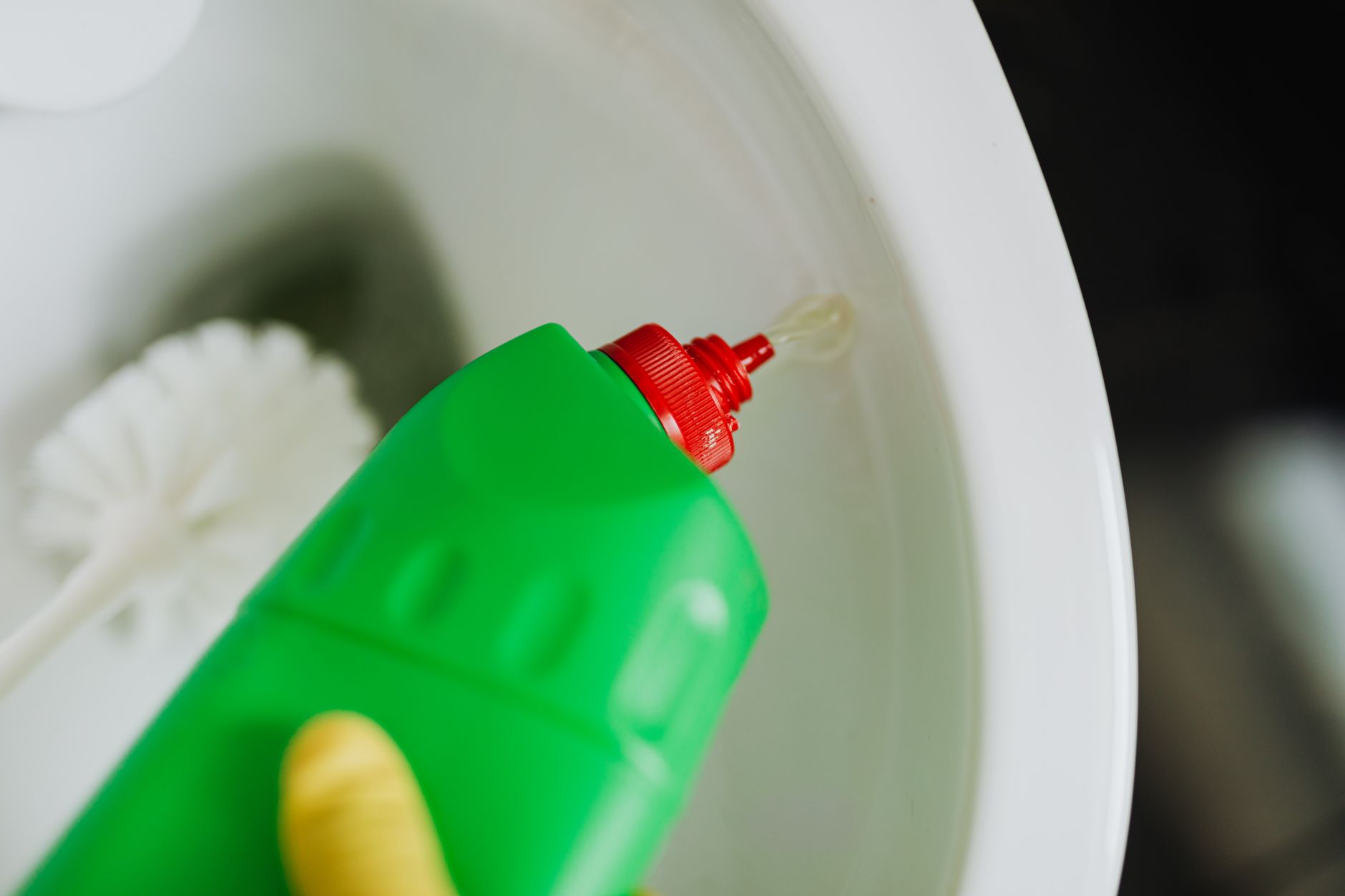 Top view of crop faceless person in yellow rubber gloves cleaning toilet with brush and pouring liquid disinfecting cleaner in toilet bowl