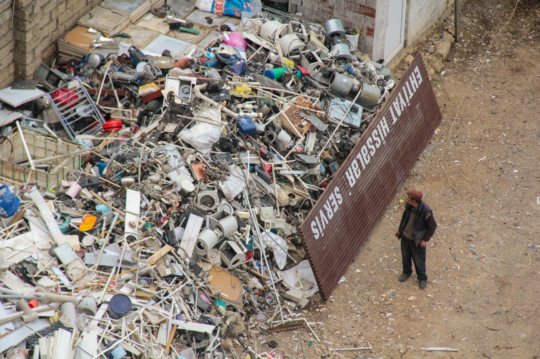 A person inspecting a large pile of scrap metal and electronic waste in an outdoor junkyard.