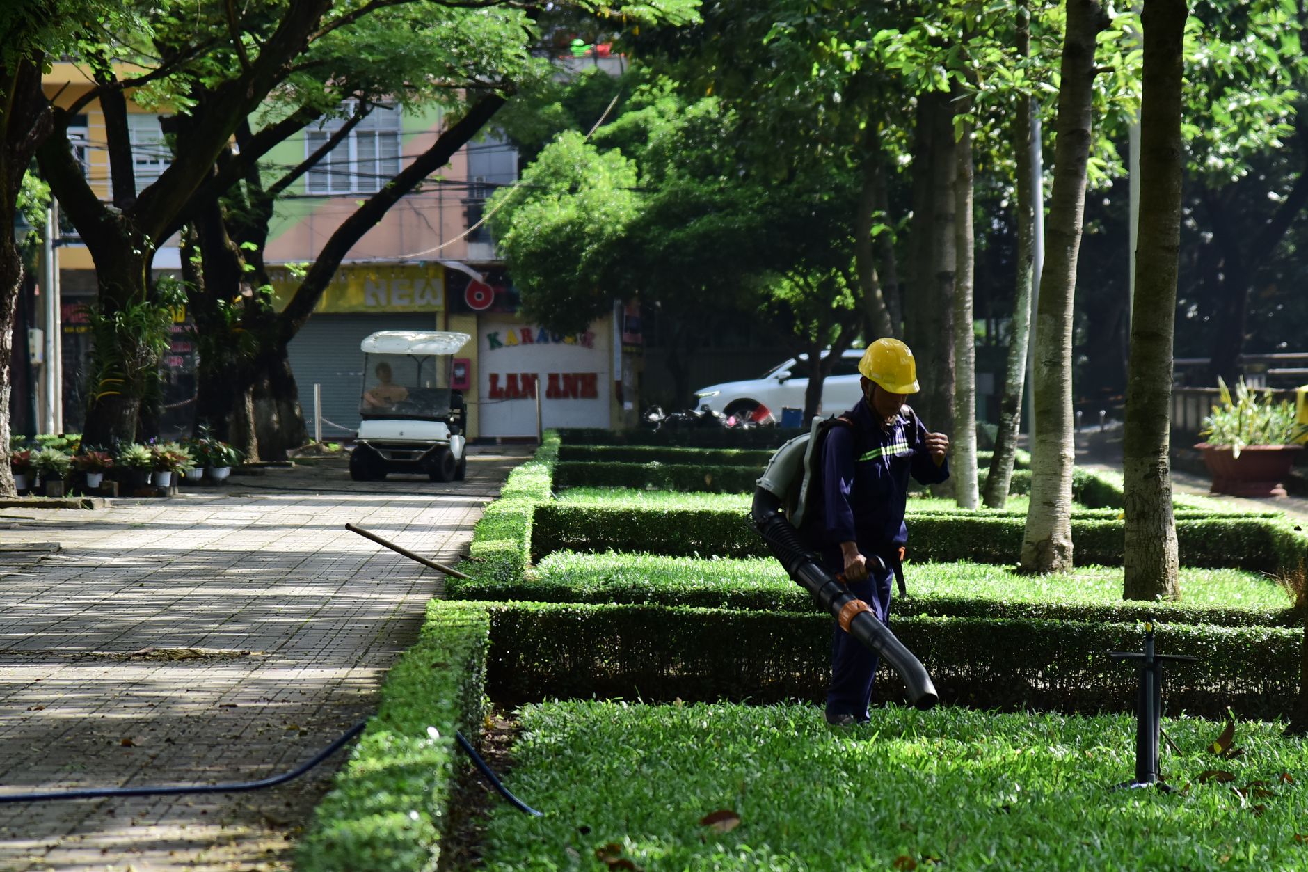 A gardener in uniform uses a leaf blower to maintain a city park's greenery, emphasizing urban cleanliness.