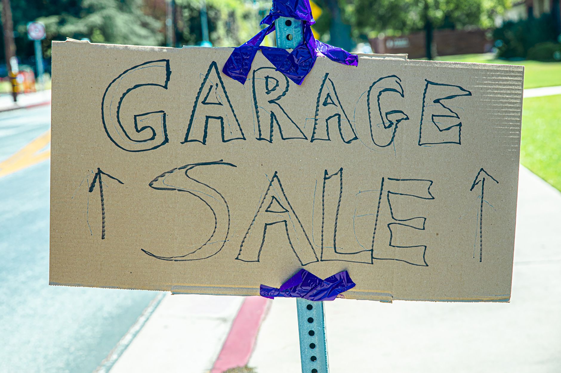 A handwritten garage sale sign taped on cardboard, displayed outdoors.