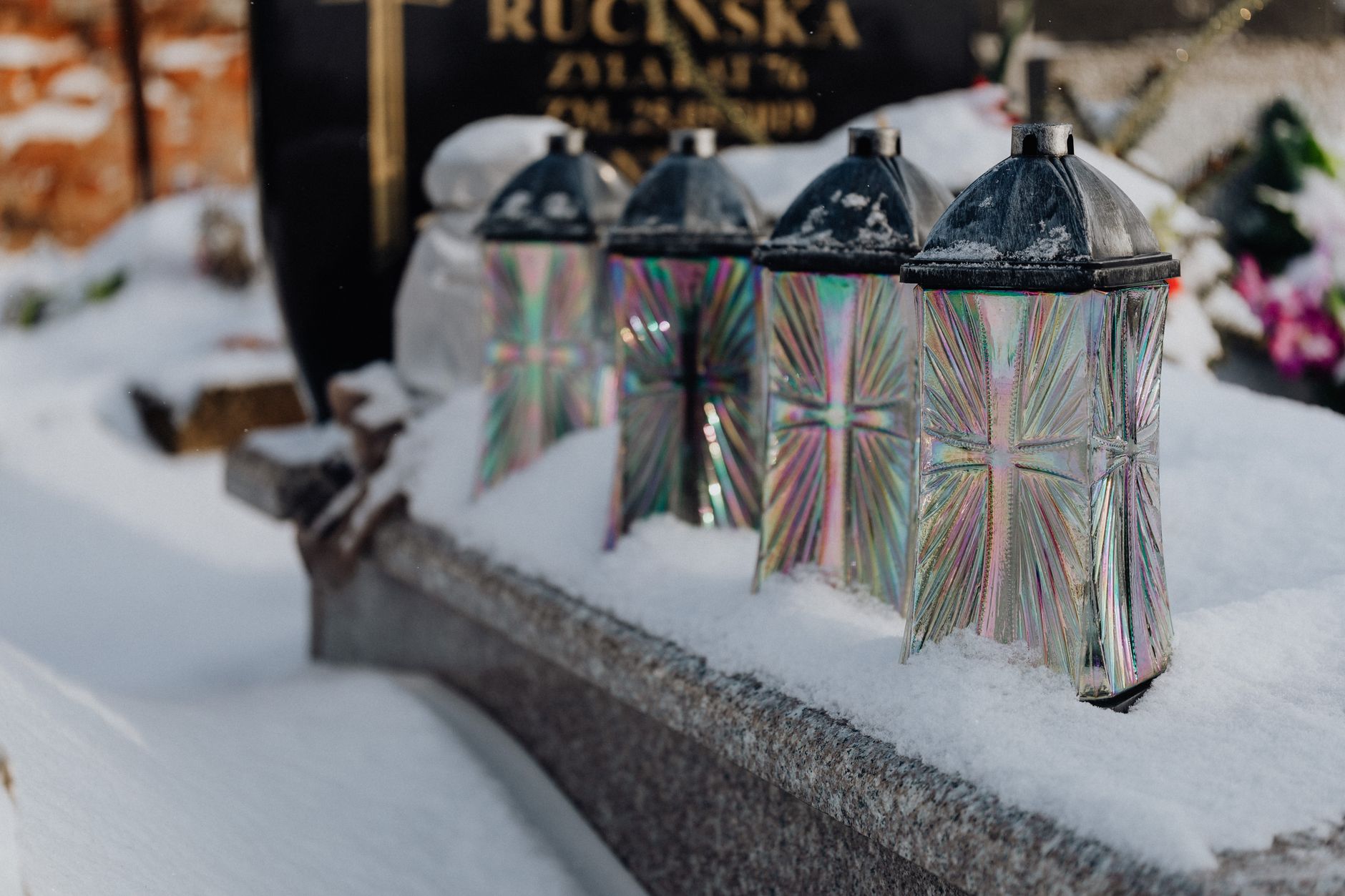 Close-up of snow-covered glass lanterns on a tombstone in a winter cemetery setting.