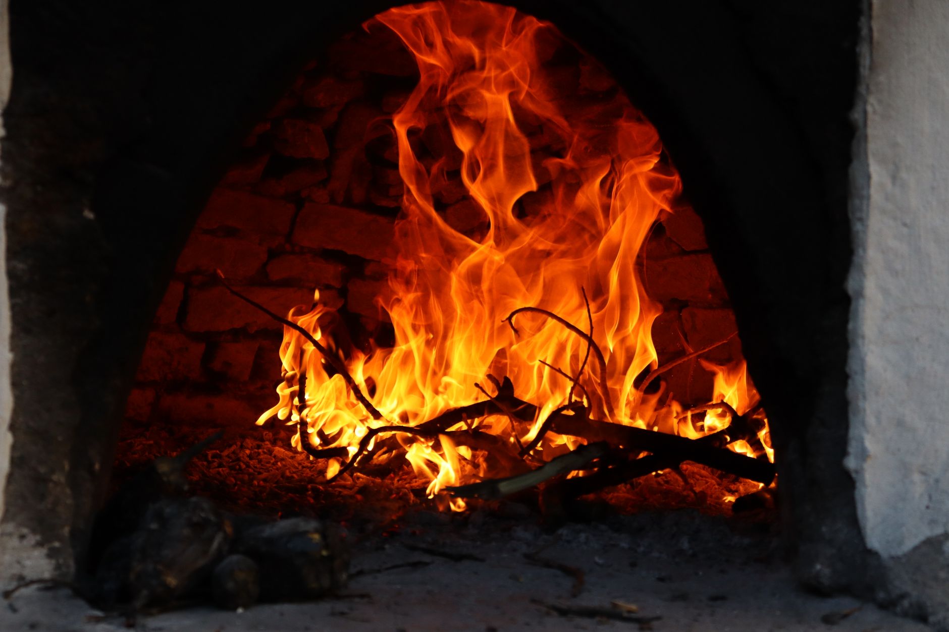 Bright flames envelop branches inside a rustic brick fireplace, creating warmth.