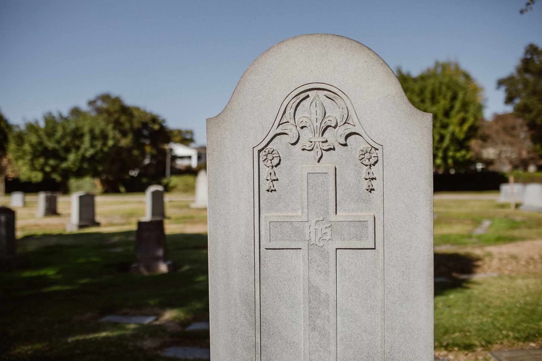 Close-up of a gravestone in a cemetery under clear skies, showcasing detailed engravings.