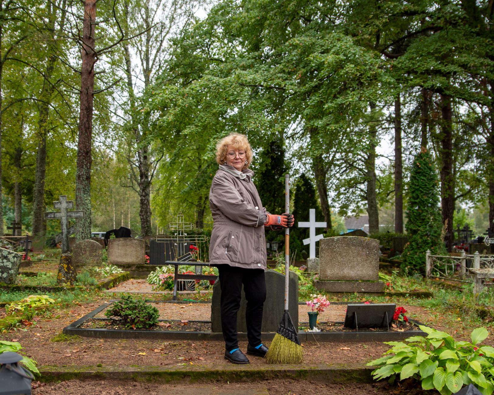 A senior woman tends to a grave in a tranquil Estonian cemetery, symbolizing respect and remembrance.