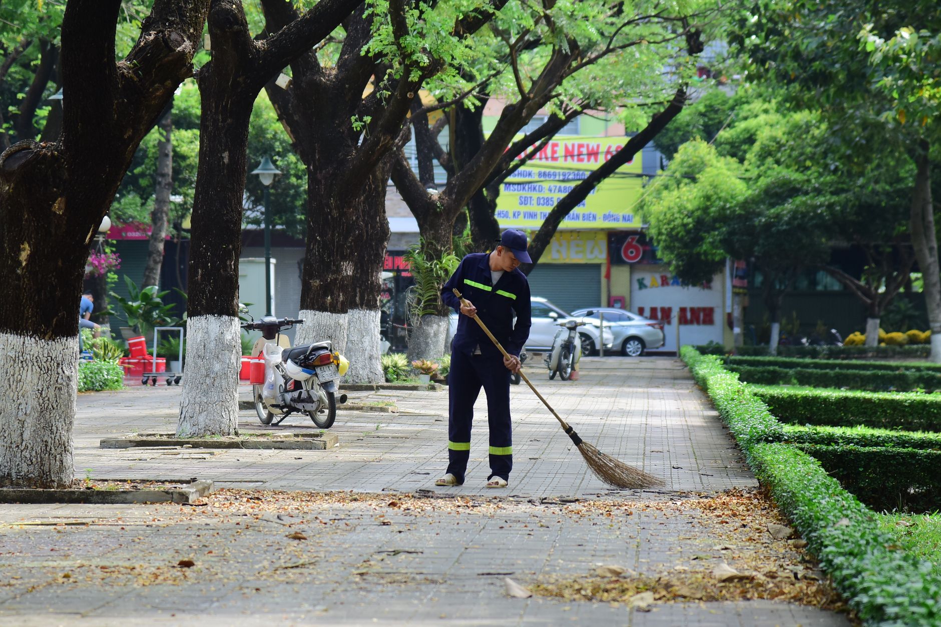 A street cleaner sweeping leaves in an urban park setting during the day.