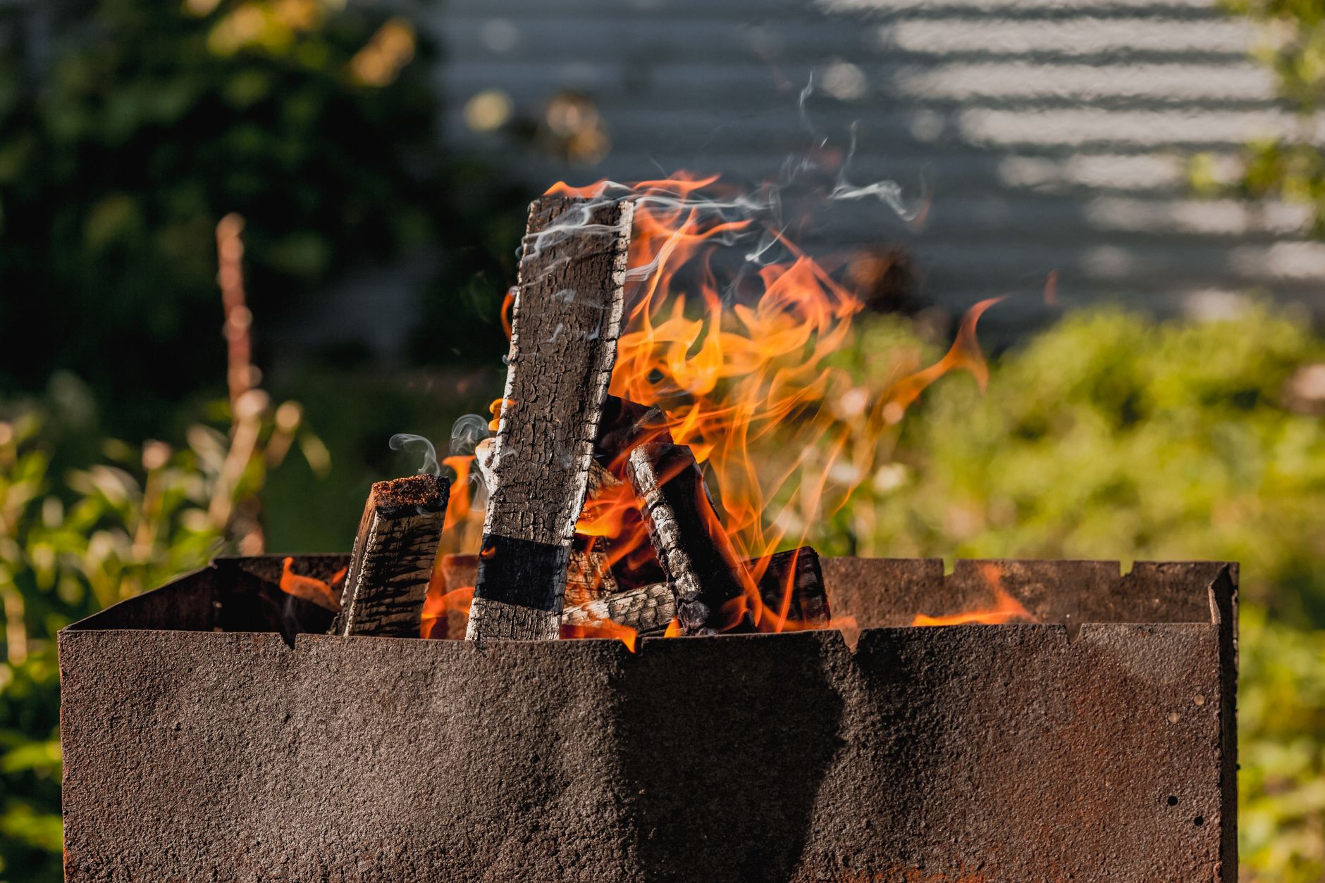 Metal brazier with burning firewood and orange flames in green garden on sunny day