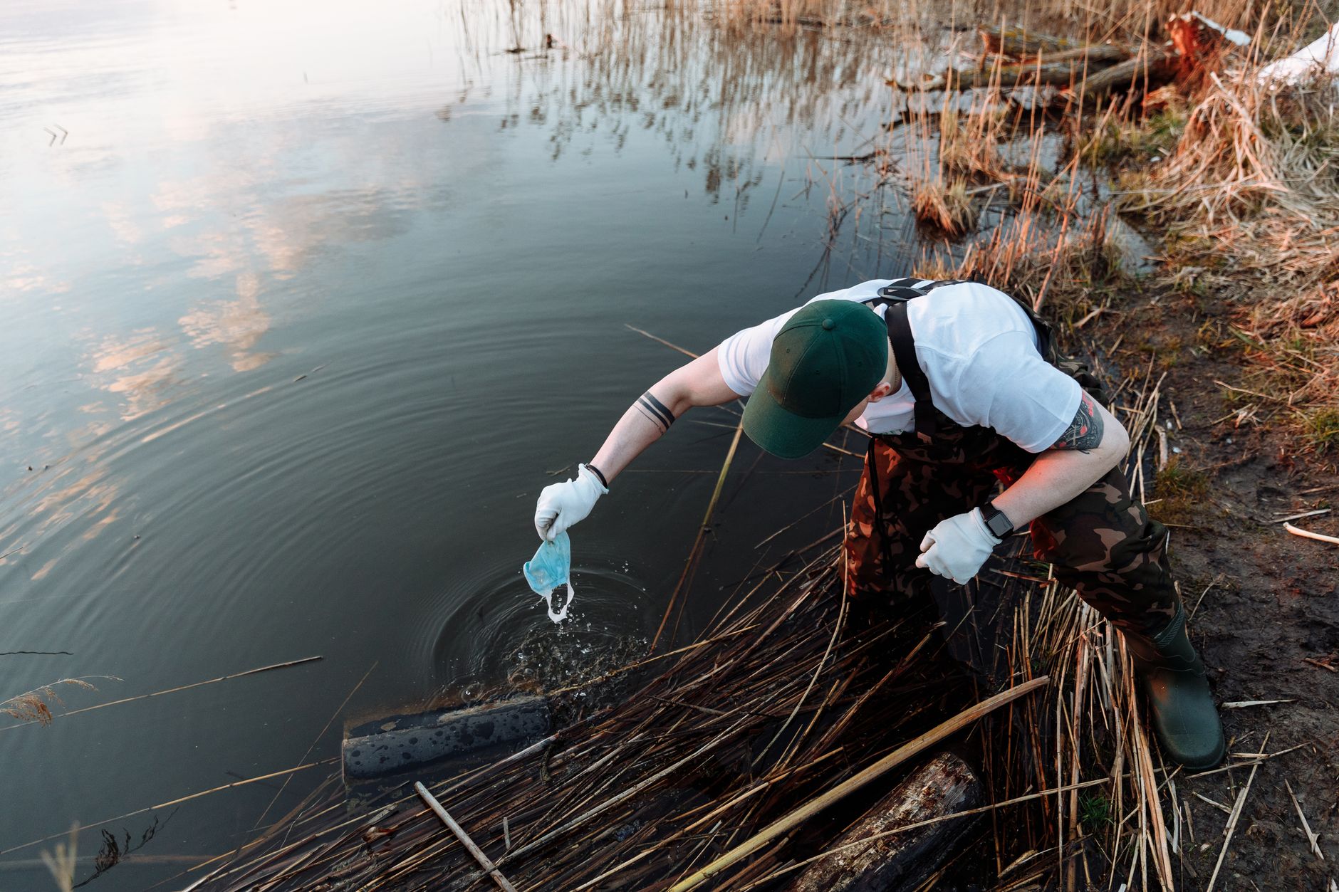 Volunteer collecting trash along a lake to promote environmental conservation.