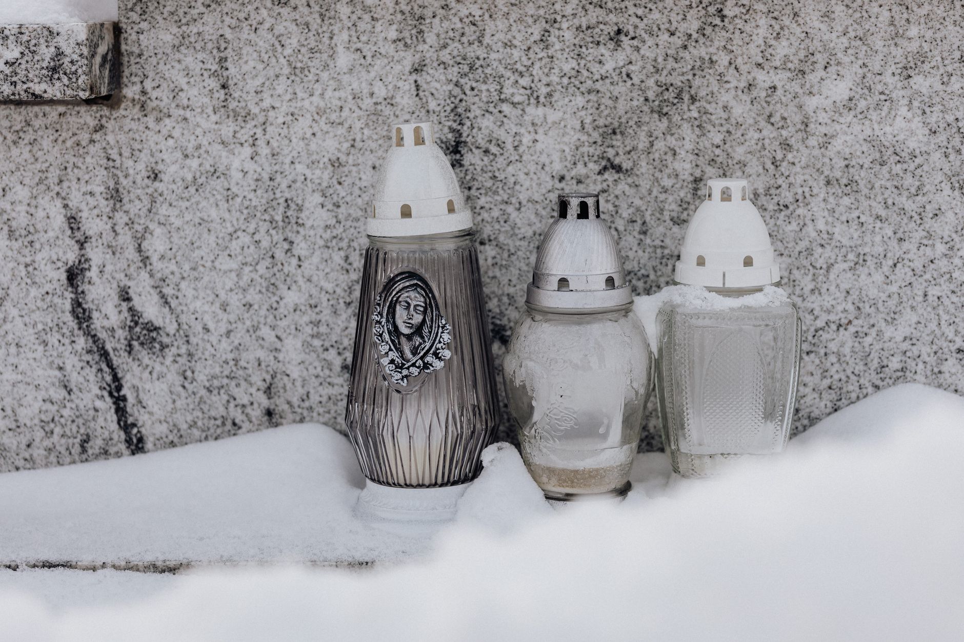 Close-up of three frosted grave candles in snowy winter setting, symbolizing memory.