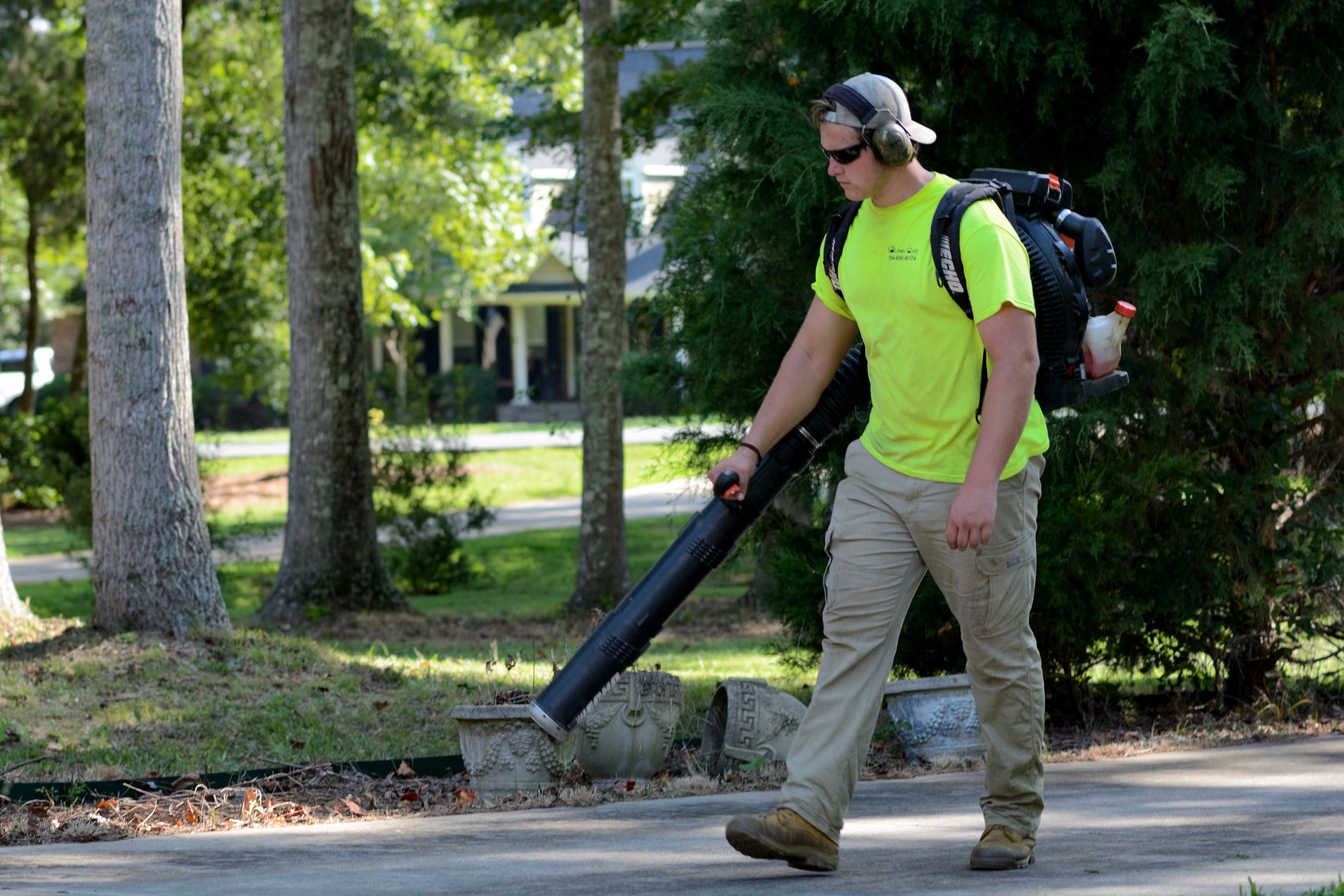 A landscaper wearing protective gear operates a leaf blower in a sunlit park, maintaining the area clean.