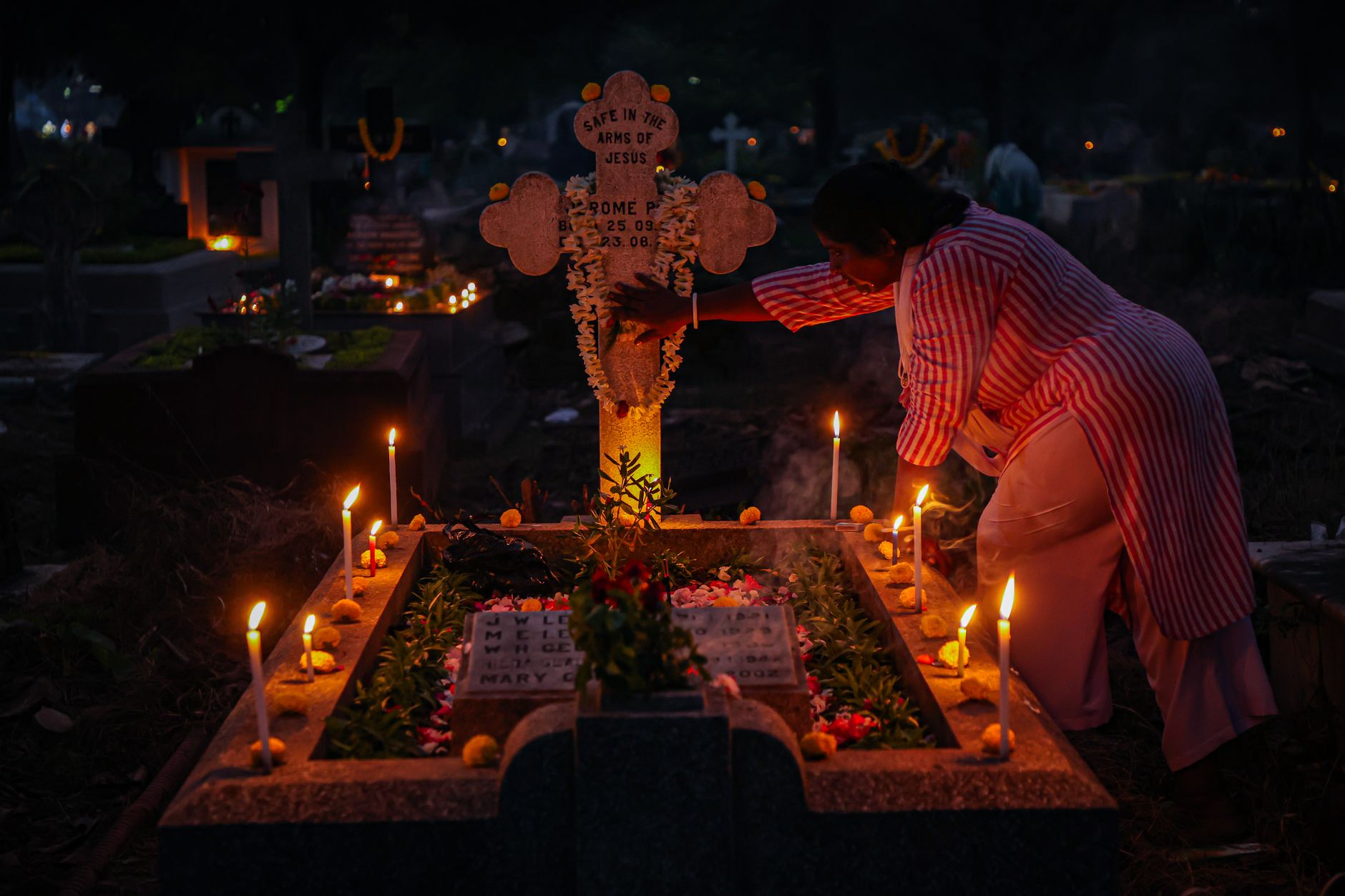 A woman arranging candles at a grave during a nighttime candlelit vigil, honoring tradition.
