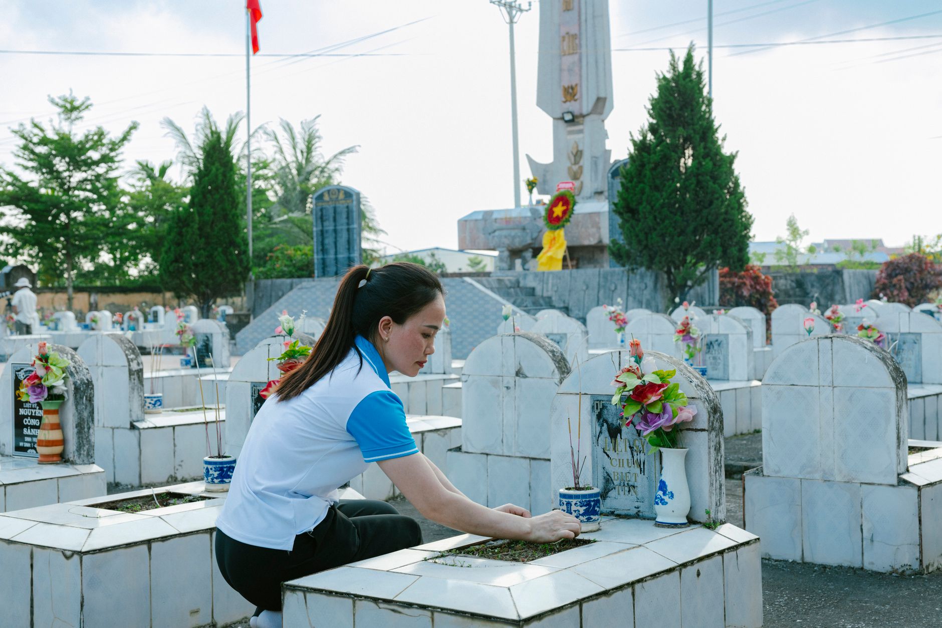 Woman tending to a grave at a cemetery, honoring the deceased with flowers and incense.