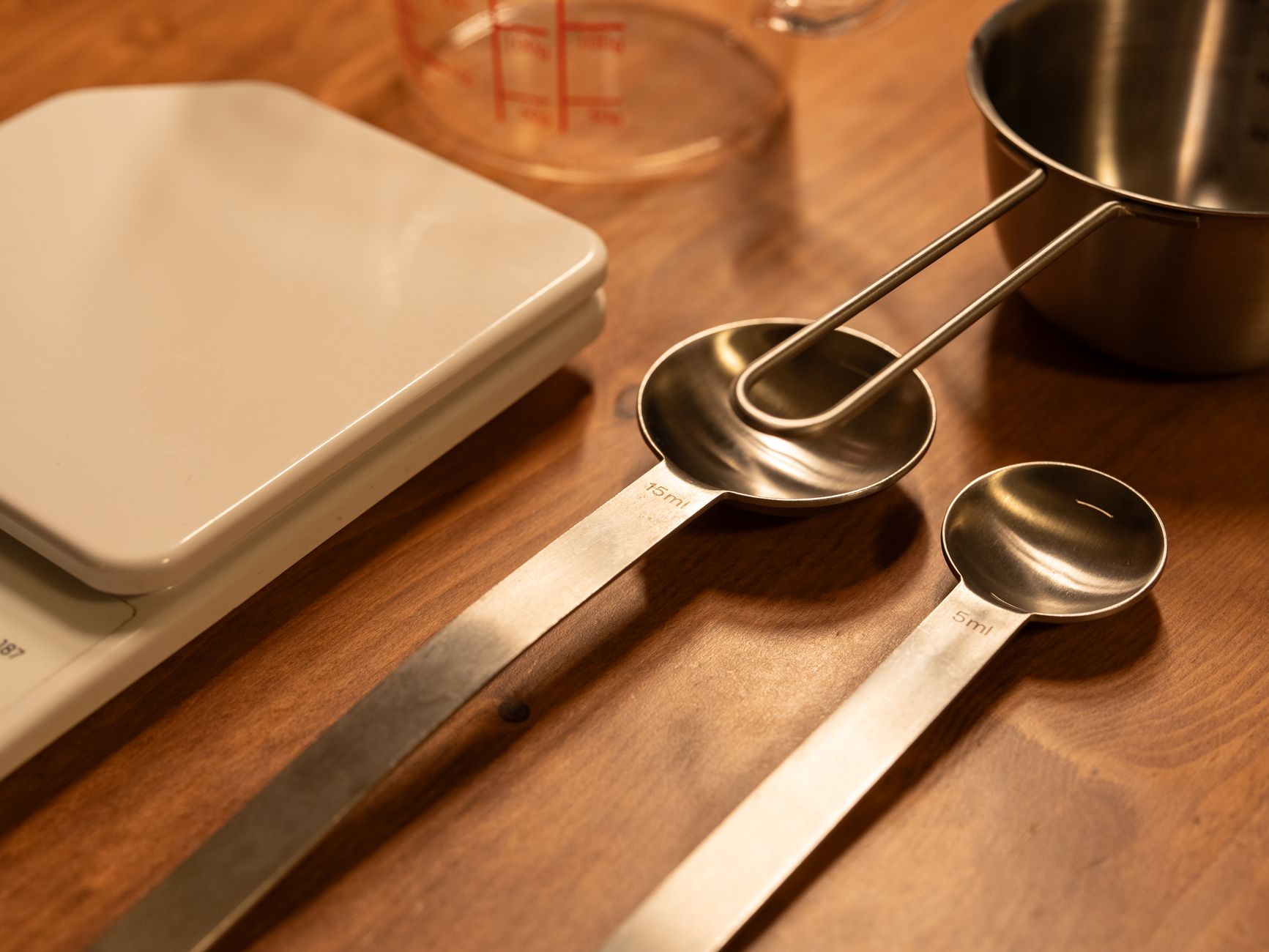 A close-up of kitchen utensils including a scale, measuring cups, and spoons on a wooden counter.