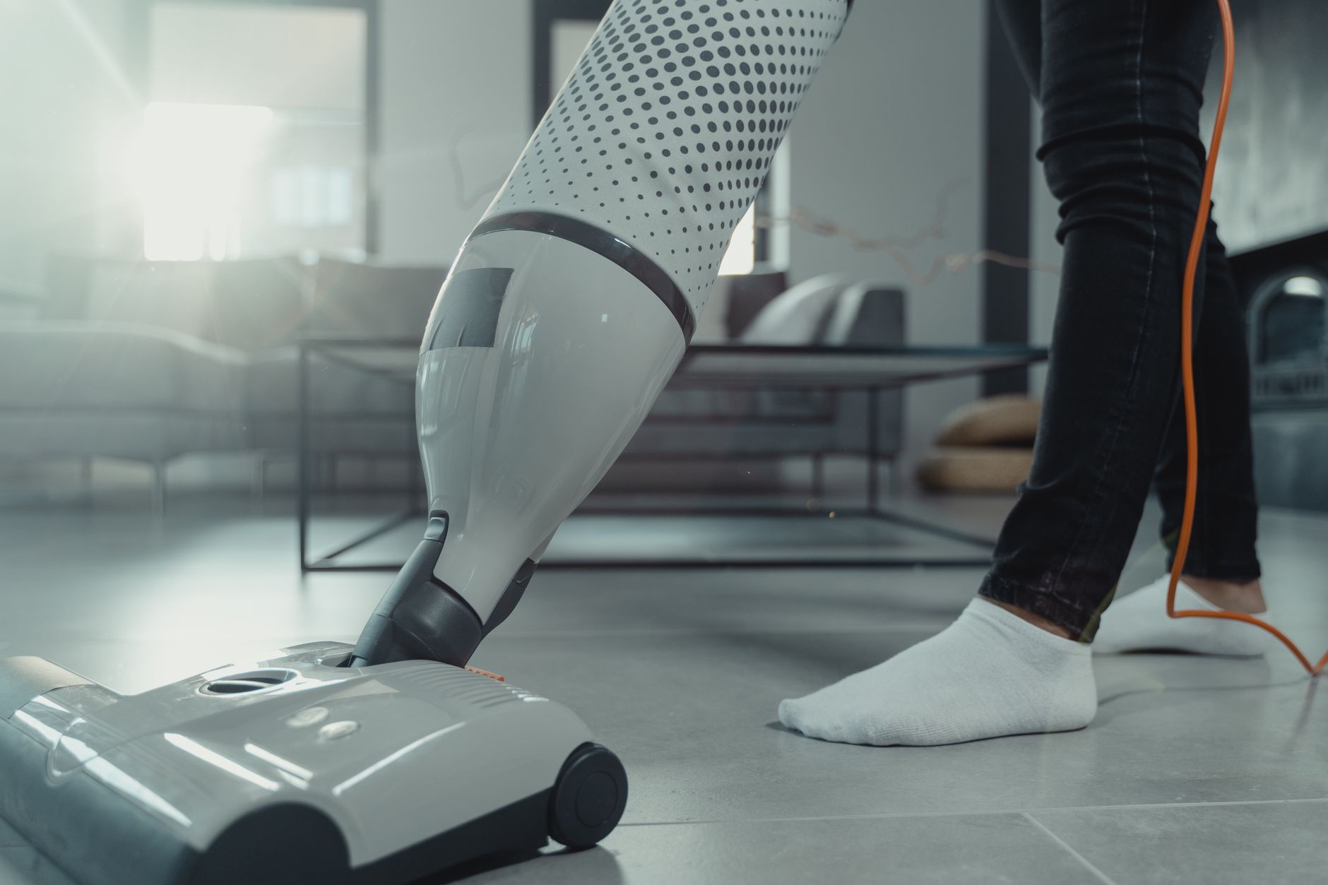 Person vacuuming a tiled floor with a modern appliance in a bright indoor setting.